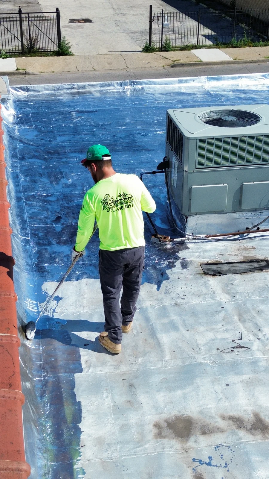 Crew member rolling roof coating beside a rooftop unit near Alsip, IL