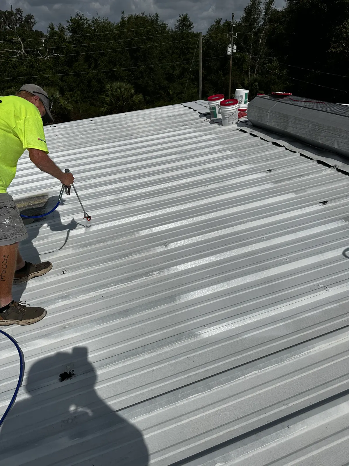 Guardian Roofing Systems crew member in safety green spray coating a metal roof